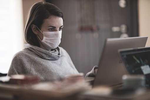 Eine Frau sitzt mit Mund-Nasen-Schutz an einem Laptop und arbeitet.